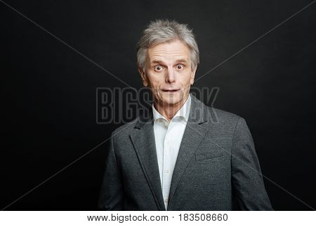 Feeling of puzzlement. Frustrated shocked aging man expressing astonishment and looking with wonder while standing isolated in black background