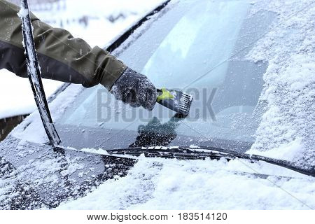 man is scraping a wind screen of a car
