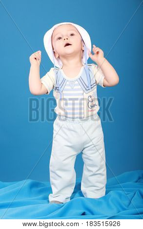 Little boy in a sailor suit. Looking up standing on blue background