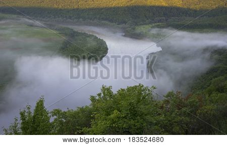 Dniester (Dnestr) river covered with mist and surrounded with green forest and fields.