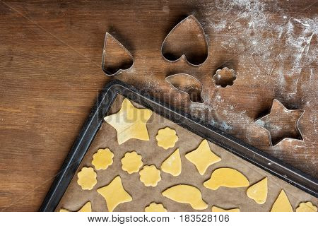 Top View Of Raw Shaped Cookies On Baking Tray And Cookie Cutters On Wooden Table