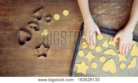 Top View Of Child With Raw Shaped Cookies On Baking Tray And Cookie Cutters On Wooden Table