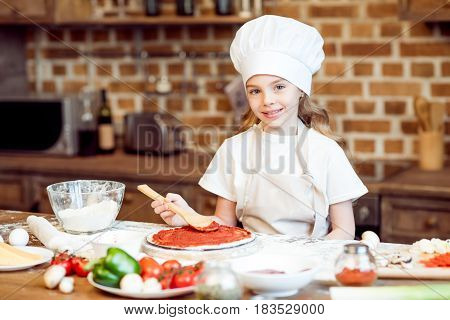 Smiling Girl Putting Tomato Sauce On Pizza Dough