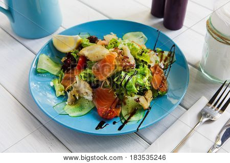 Restaurant healthy food, seafood salad closeup. Salmon and cod fish salad with vegetables and lettuce on blue plate. Appetizing dish served with sauce, dinner meal. Selective focus