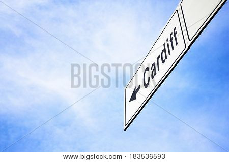 White signboard with an arrow pointing left towards Cardiff Wales - the capital city United Kingdom against a hazy blue sky in a concept of travel navigation and direction