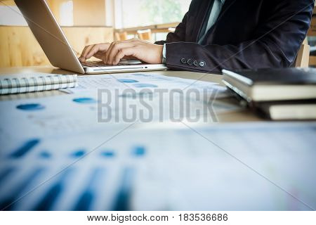 Young business manager working at office with laptop and financial data documents on his desk.
