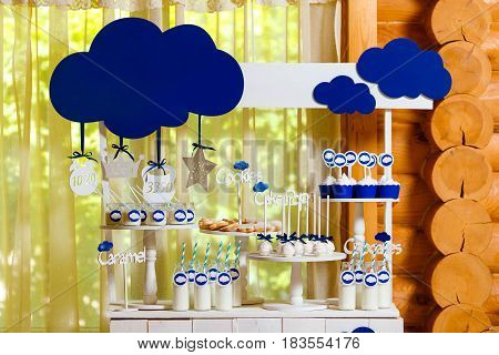 Candy bar on baby's christening party with a lot of different candies and beverages. Decorated in blue colors clouds theme indoor