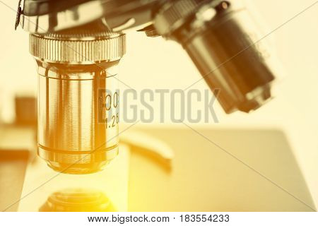 Close up of objective lenses with a microscope slide on a stage and clip. Basic optical microscopes can be very simple and there are many complex designs aim to improve resolution and sample contrast.