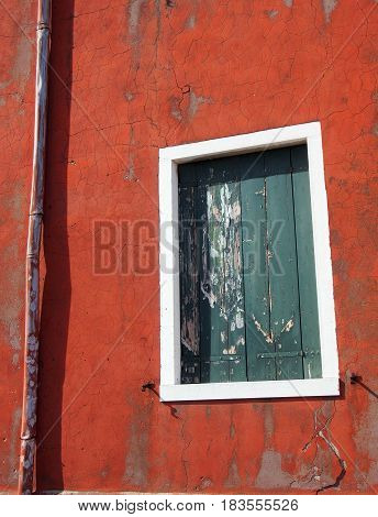 old green suttered window with peeling paint on a red exterior wall