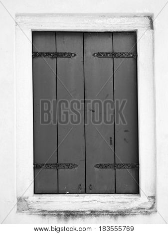 grey shuttered window with metal hinges in a white wall