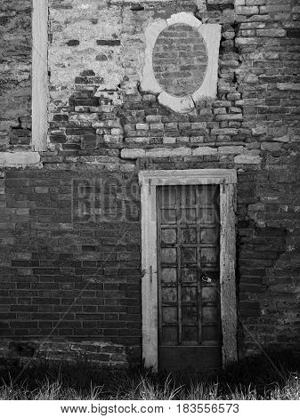 Old wooden paneled door with peeling paint and rusting hinges in an ancient brick wall