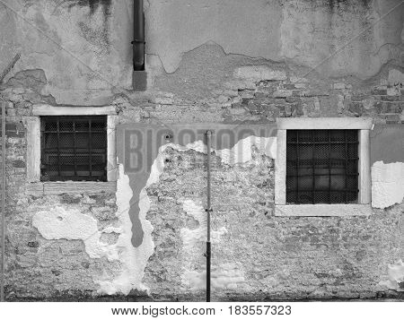 old weathered brick wall with broken plaster and two windows