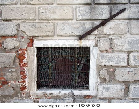 small window in a white exterior wall with brick repairs and metal bar