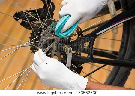 Closeup hand wearing white glove holding sponge rubbing on metal bicycle chain, mechanical repair concept.