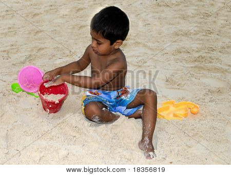 eine gut aussehend indischer Kind machen eine Sand Burg am Strand