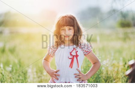 Cute little girl in a white dress on a field in sunlight.