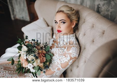 Beautiful bride in a lace dress with an original wedding bouquet in a vintage interior.