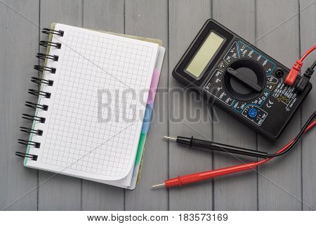 Multimeter On A Wooden Background Next To An Empty Notepad. Empty Space.