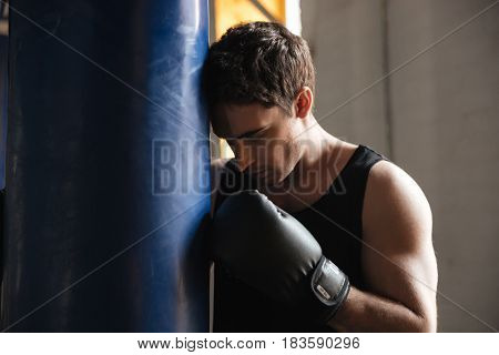 Pensive sportsman boxer thinking about training in gym near punchbag