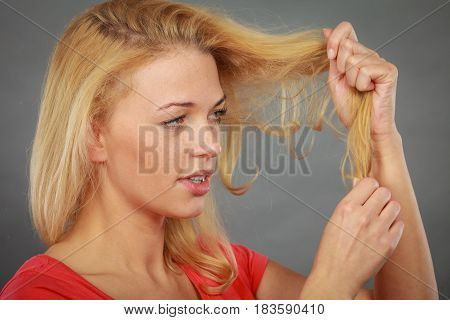 Haircare health problem concept. Unhappy sad woman looking at damaged split ends on her blonde hair