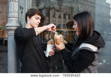 Young man trying to eat burger of his sister near cafe