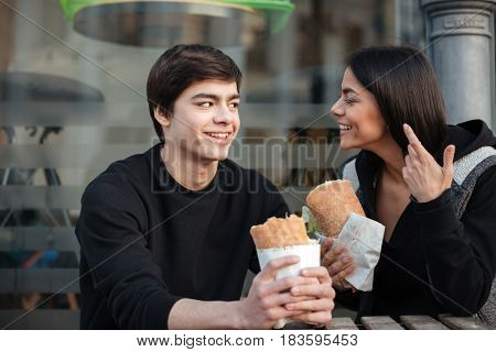 Young man with burger listening his cute sister in the street near cafe