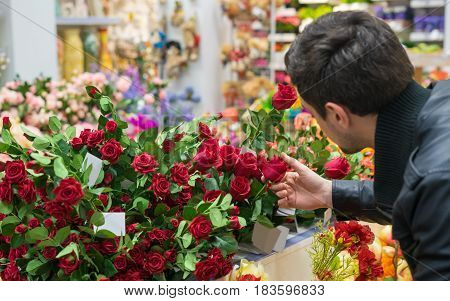 Handsome man choosing red roses at a florist shop for his girlfriend. Romantic present