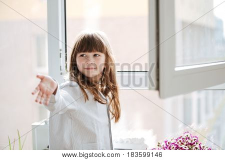Little smiling girl reaching out hand near window in room