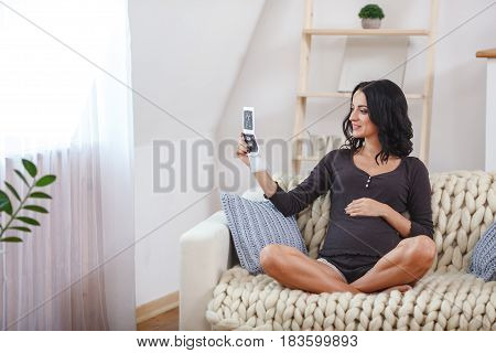happy beautiful bruntte pregnant woman relaxing on sofa with echo scan in hands