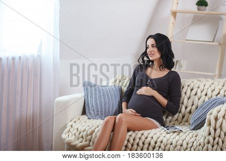 happy beautiful bruntte pregnant woman relaxing on sofa with echo scan