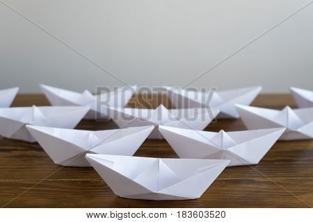 Origami white paper boats on a wooden table, soft focus.