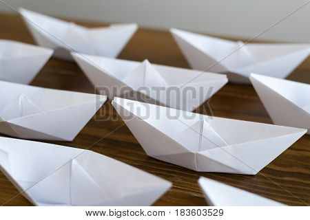 Origami white paper boats on a wooden table, soft focus.