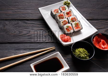 Eating rolls at sushi restaurant. Japanese food, maki on dark background. Set with soy, gignger and chopsticks. Closeup on black wood