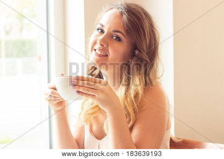 A beautiful young woman sitting in a cafe. Girl drinks Cappuccino.