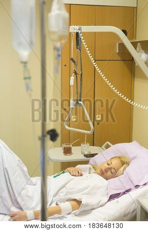 Bedridden female patient lying in hospital bed, recovering after surgery.