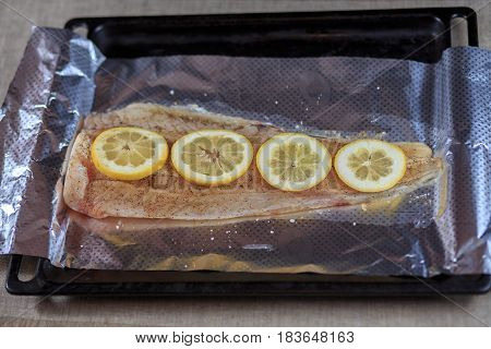 Fillet Is Fresher Than Fish In Seasoning Under A Lemon On A Foil On A Black Background