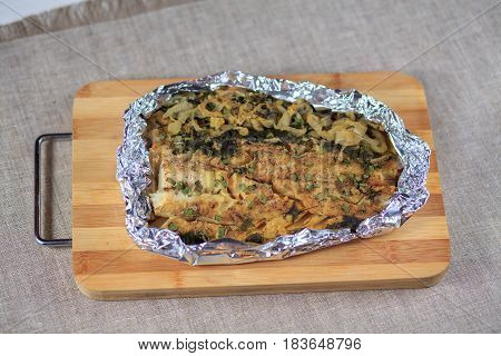 Fillet Of The Baked Fish In Seasonings And Greens In A Foil On A Board