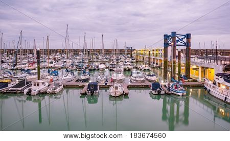 Boats yachts and fishing boats moored at Brighton Marina docs on a cloudy day.