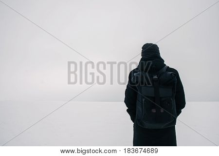 back hipster young man with a black backpack traveling in winter on the frozen pond