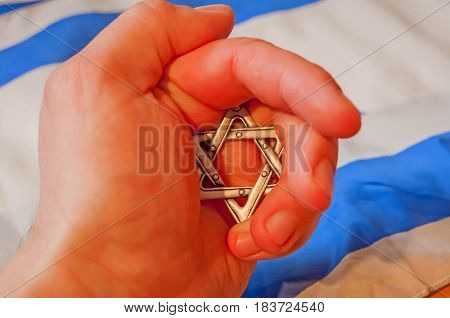 Hand holding a Star of David ("Magen David") with Israeli flag on the background. Hidden Jewish identity concept.