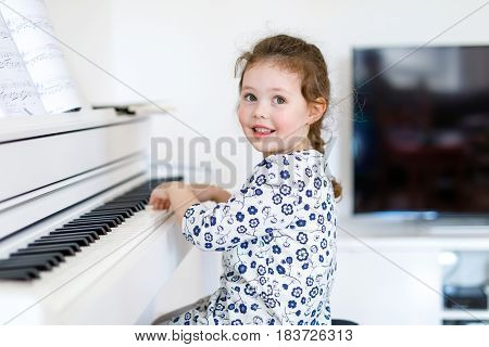 Beautiful little kid girl playing piano in living room or music school. Preschool child having fun with learning to play music instrument. Education, skills concept.