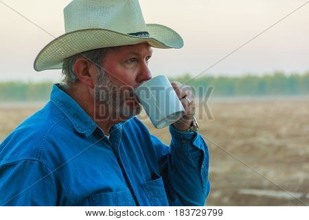 Senior in cowboy hat drinking coffee while contemplating field in morning