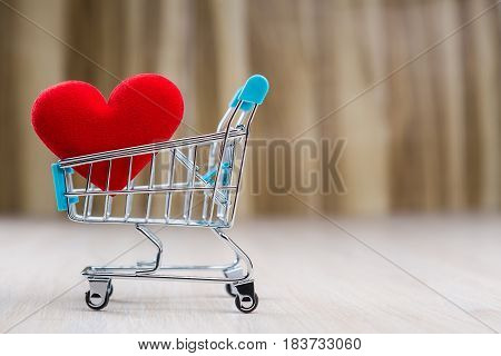 Red heart in the shopping cart on the wooden floor.