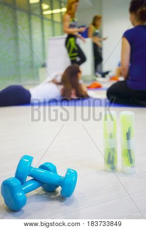 Two skipping ropes, dumbbells are on floor, three women are in hall for fitness out of focus