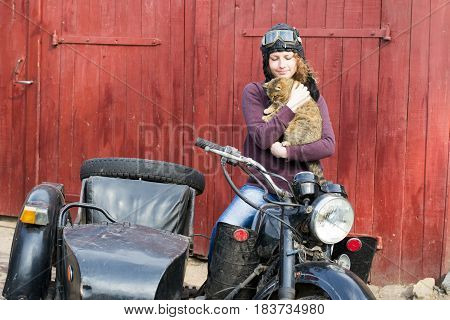 Photo of girl on vintage motorbike in pilot cap with cat