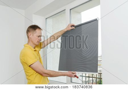 Man is holding fabric window blind gray.
