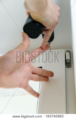 Male is drilling a hole in the window frame.