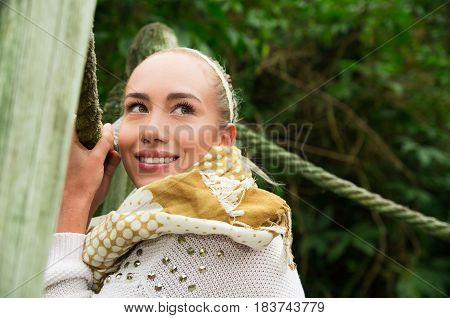 Close up shot if young smiling blond girl sitting in a walking wooden bridge looking peaceful