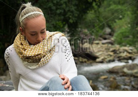 Happy young girl sitting by the river rocks in a forest enjoying the quietness