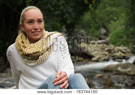 Happy young girl sitting by the river rocks in a forest enjoying the quietness
